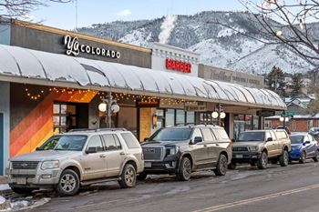 A row of suvs are parked in front of a barber shop and a yoga studio.